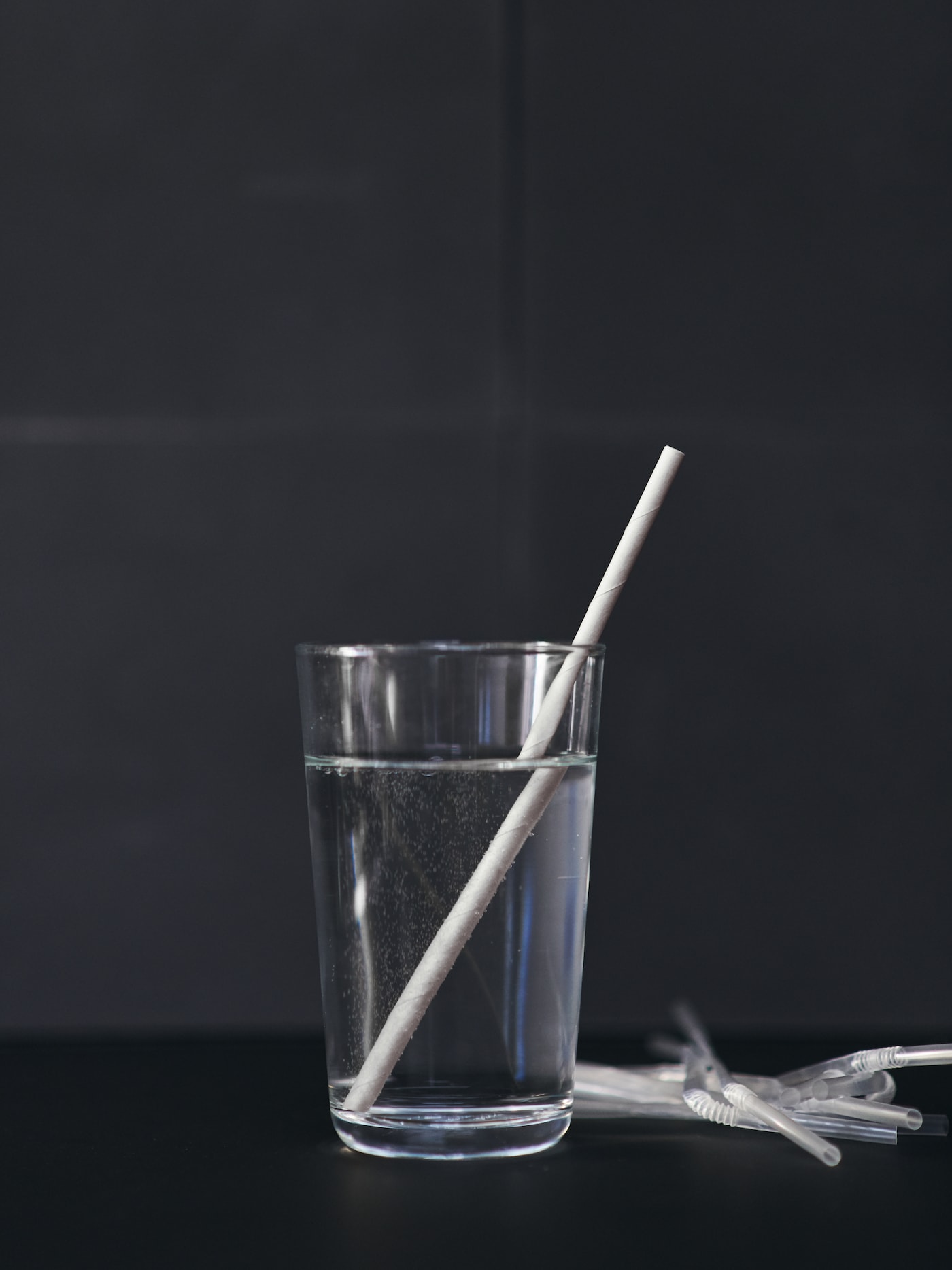 装满水的玻璃杯中放着FÖRNYANDE 菲漾德 吸管,背景中是一次性塑料吸管。