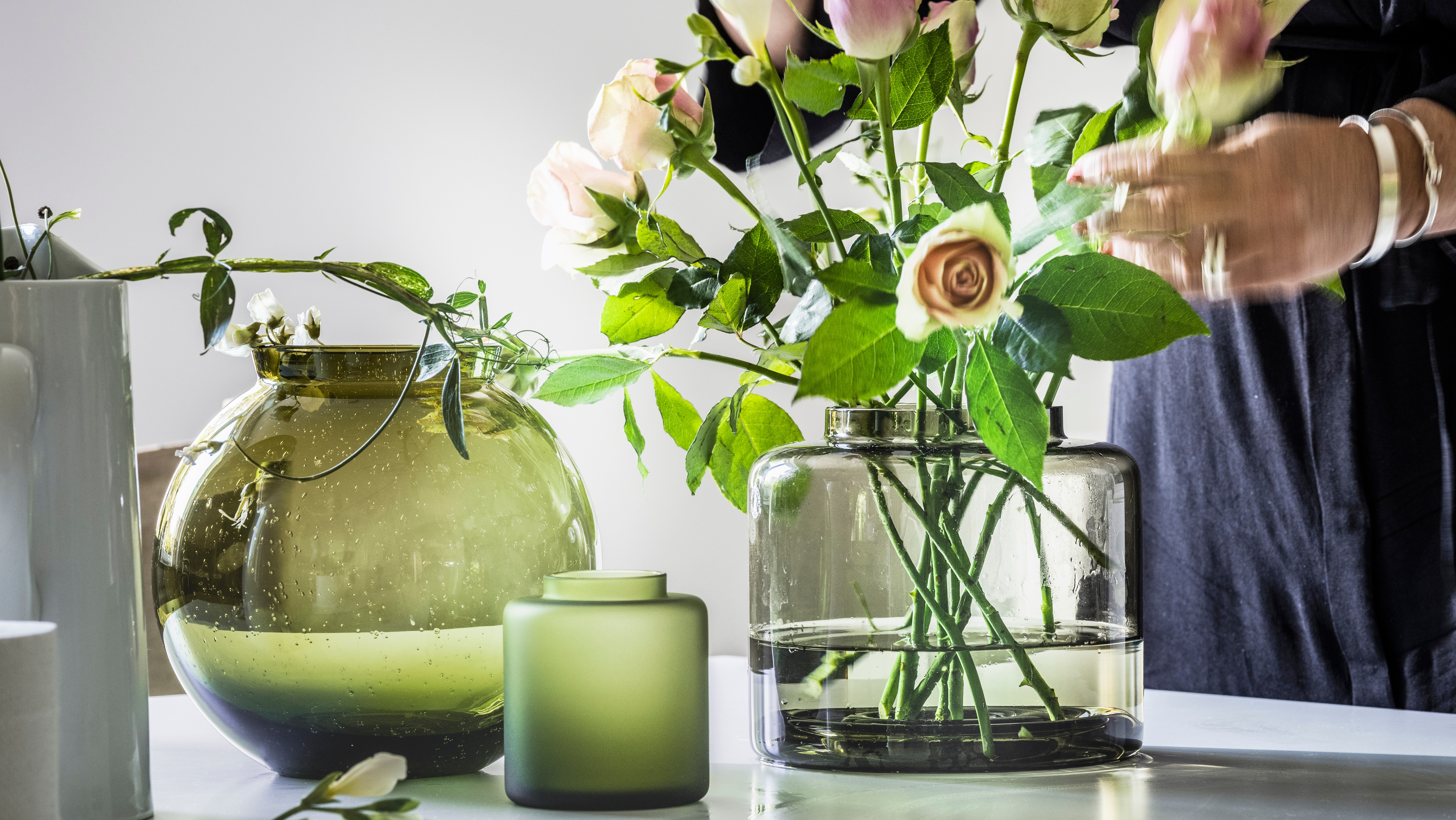 A person is arranging flowers in a KONSTFULL vase made of clear glass standing next to two more KONSTFULL vases.