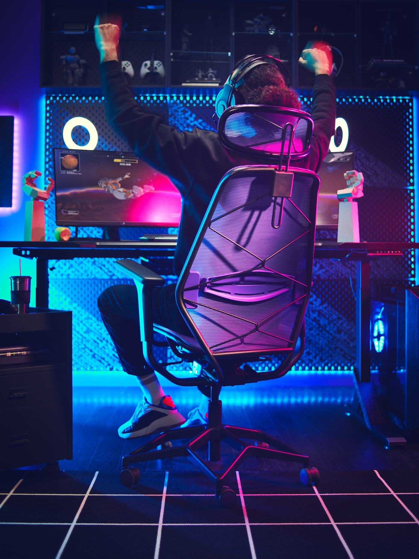A young man with headphones on sits in a purple STYRSPEL gaming chair and holds his hands up in the air.