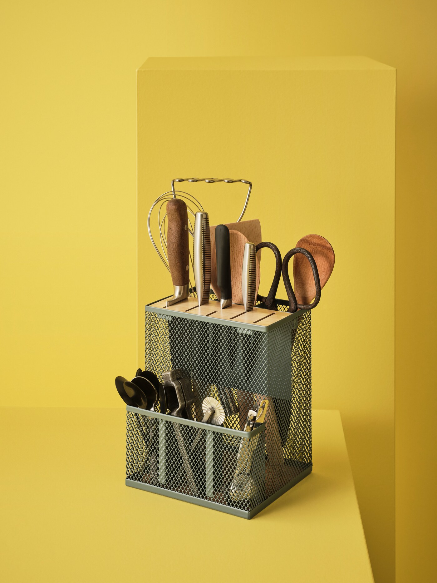 A VIMPELFISK knife block is filled with utensils, knives, wooden spatulas and cutlery, and sits on a yellow pedestal.