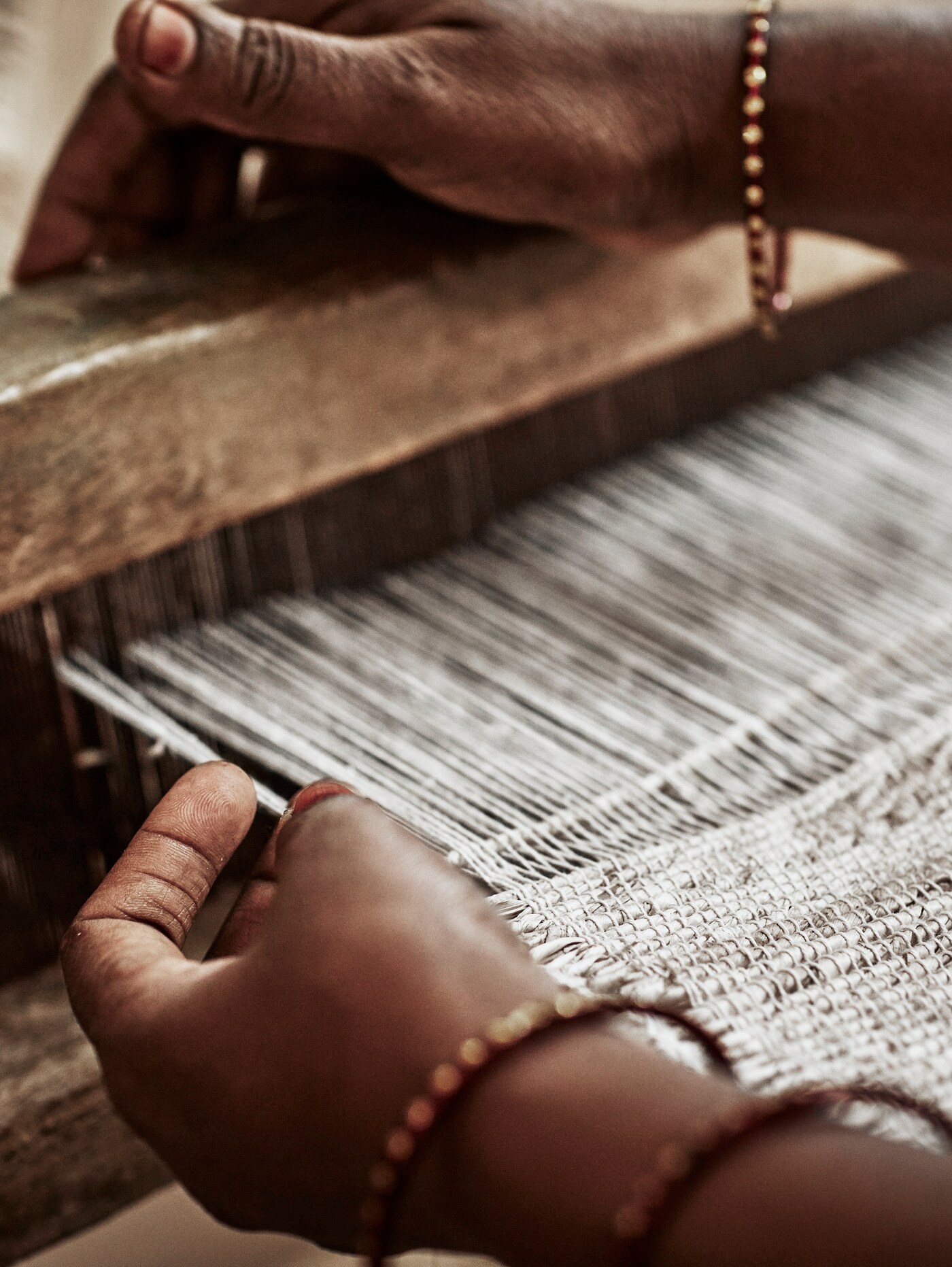 The hands of an Indian weaver adorned with several copper bracelets, weaving a rug on a loom.