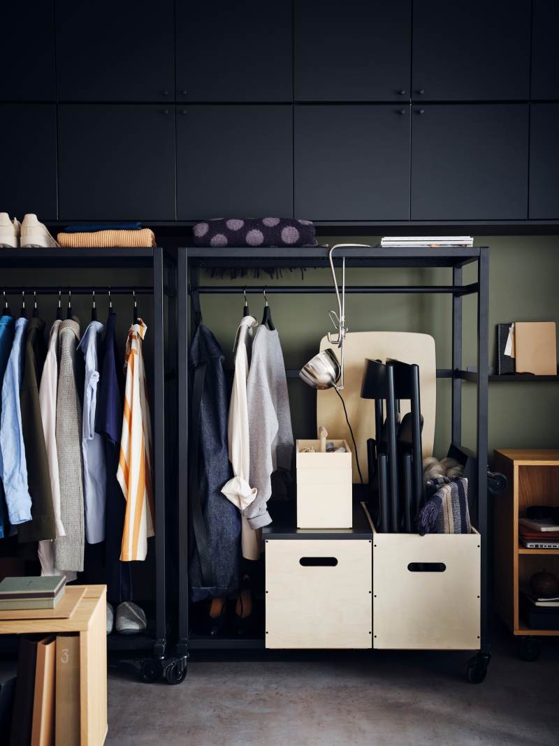 Black RÅVAROR storage units on castors are filled with clothing and RÅVAROR boxes, with a RÅVAROR throw lying on top.