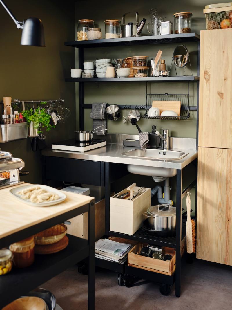 A RÅVAROR mini-kitchen with a hanging dish drainer and hooks, is filled with crockery and a RÅVAROR storage box.