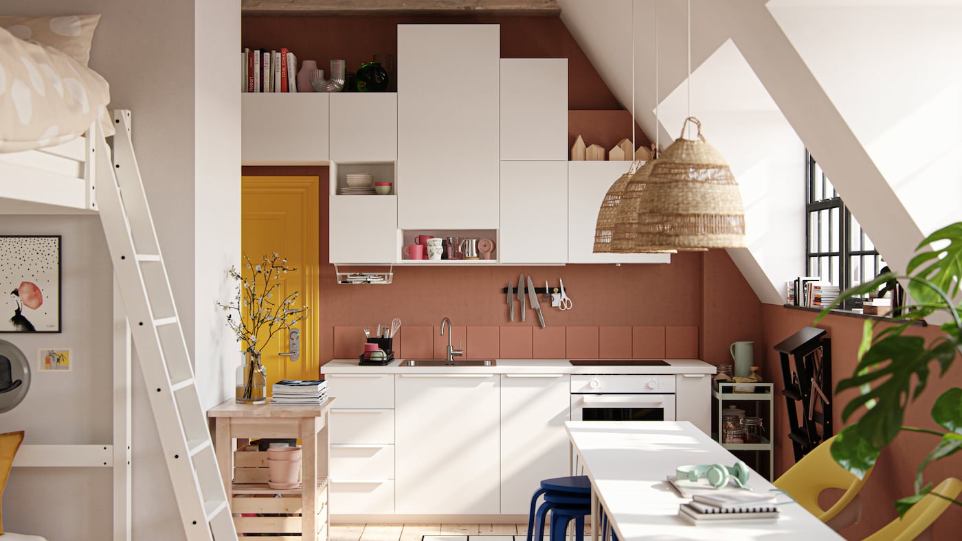 A studio space with large industrial-style windows, dark terracotta-coloured walls and white VALLSTENA kitchen fronts.