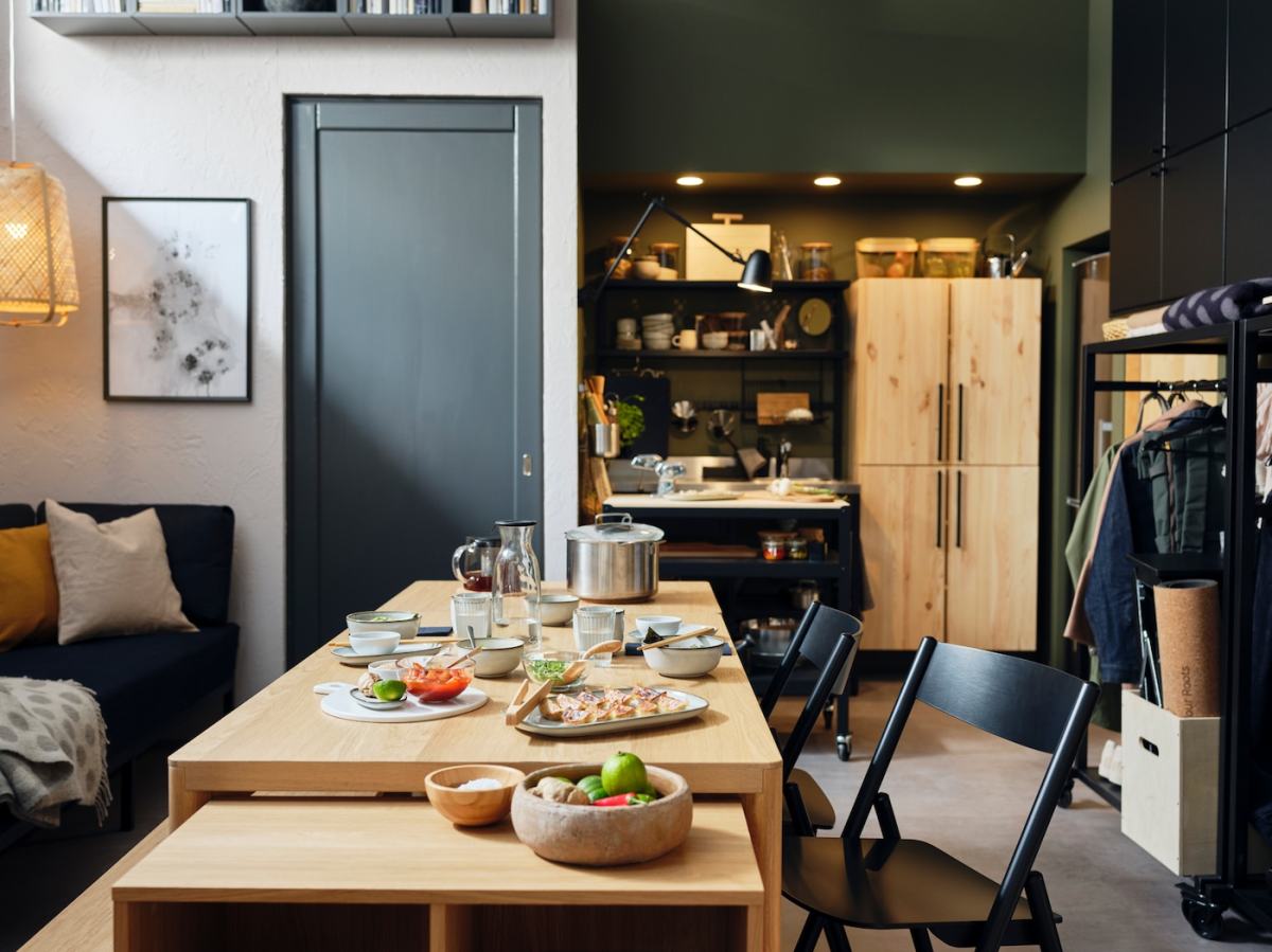 A RÅVAROR table, storage unit, and folding chairs are situated in the middle of an apartment. There is crockery on the table.